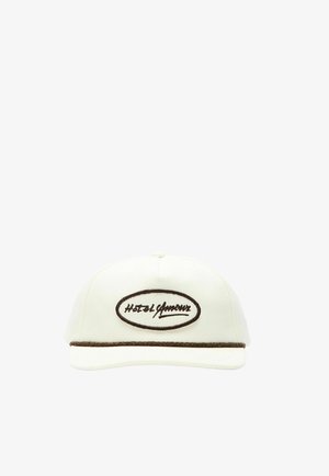 Hvit caps med buet brem, brun kant over bremmen og et ovalt merke med kursiv tekst.