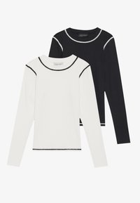Dvě dlouhé rukávy v bílé a černé směsi bavlny, s kontrastním šitím na výstřihu a spodním okraji. Jednoduchý, dobře padnoucí design.