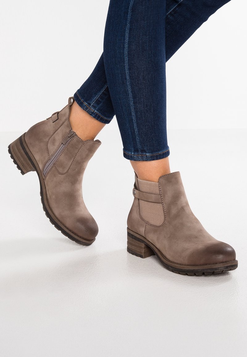 Bottines en suède marron avec un bout rond, des panneaux latéraux élastiques et un talon carré texturé. Le design comprend une fermeture éclair sur le côté et des accents cousus.