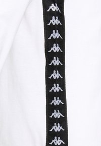 Weißer Pullover mit schwarzem Seitenstreifen, der wiederholte silberne Logodesigns zeigt. Das Material scheint aus Baumwolle oder ähnlichem zu sein und hat eine glatte Textur.