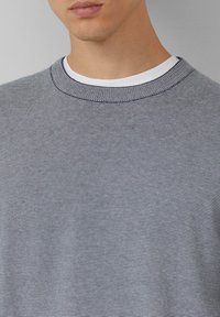 Gestreepte gebreide trui in grijs en wit. Voorzien van een ronde hals met geribbelde accenten en een gestructureerde stof. Close-up van het borstgedeelte.