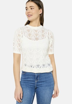 Top blanc en maille à manches courtes présentant un motif en dentelle ouverte, avec un col rond et une coupe cropped, assorti à un jean bleu.