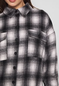 Randig flanellskjorta i svart och vitt med krage, knappstängning, två bröstfickor och mjuk textur.