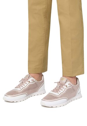 Sneakers in rete traspirante rosa chiaro con accenti bianchi, dotati di lacci, dettagli perforati e suola testurizzata. Pantaloni beige visibili.