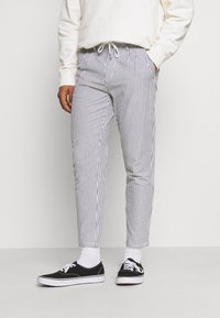 Stribede bukser i hvid og marineblå, lavet af et stof med en glat tekstur. Tapered fit med elastisk talje og sidelommer. Båret med sorte sko.