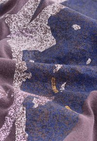 Flerfärgat tyg med nyanser av lila, blått och brunt, med ett texturerat, abstrakt mönster av oregelbundna former och accenter i rosa och gult.