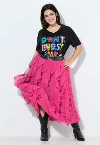 Camiseta negra con texto colorido que dice "NO ME REVIENTES," combinada con una falda rosa con volantes y botas de vaquero negras. Tela texturizada y diseño en capas.