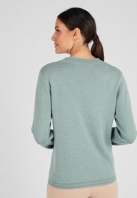 Maglione a maniche lunghe in un leggero teal, realizzato in morbido materiale a maglia. Presenta un collo rotondo e bordi a costine. Texture liscia con dettagli minimi.