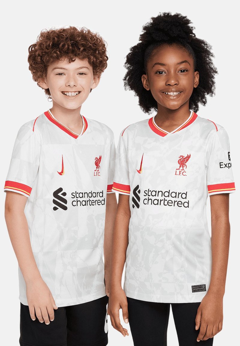 Maglietta bianca del Liverpool FC con accenti rossi, caratterizzata da un colletto a V, logo, testo dello sponsor e un motivo testurizzato. Indossata da un ragazzo e una ragazza.