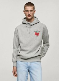 Felpa grigia con stampa frontale di una mela rossa e il testo "NEW YORK". Presenta coulisse, una vestibilità rilassata e polsini a coste. Indossata con jeans azzurri chiari.