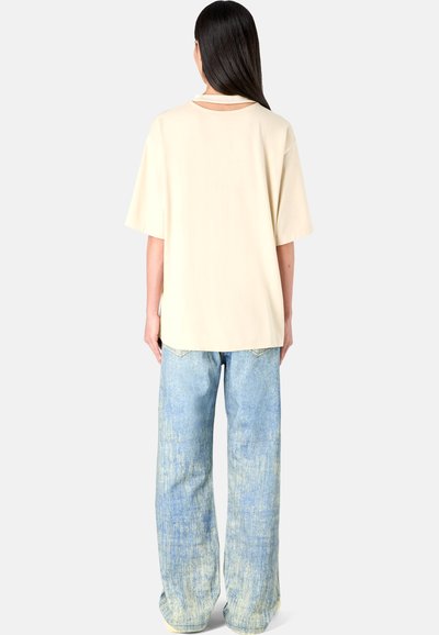 Cream t-shirt with short sleeves and back slit, paired with loose light blue jeans featuring a faded texture and straight leg design.