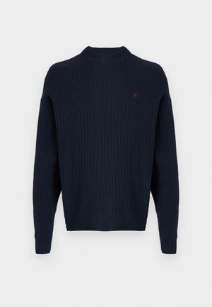 Mornarsko modra pulover z rebrastim vzorcem in visokim ovratnikom, z dolgimi rokavi in majhnim rdečim logotipom na prsih. Mehka tekstura, sproščen kroj.