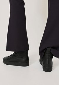 Black high-top boots made of leather with a textured finish, featuring lace-up design and a thick rubber sole. Accented with a pull tab.