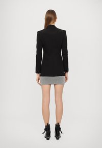 Blazer nero su misura con spalline, abbinato a una mini gonna grigio e bianco a righe. Il modello indossa stivaletti neri alla caviglia con fiocchi.