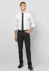 Wit overhemd, zwarte stropdas, zwarte broek en zwarte sneakers. Het overhemd heeft twee borstzakken; de broek heeft een slim-fit model. Gladde structuren overal.