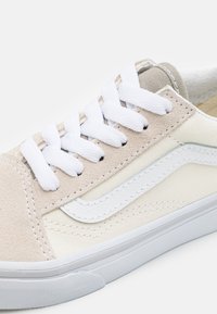 Zapatillas con una parte superior de gamuza y lona beige, cordones blancos y una suela de goma blanca con un acabado texturizado.