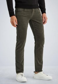 Hlače od kordura u maslinasto zeleni boji sa slim fit krojem, s prednjim džepovima i suptilnom oznakom. Uparene s bijelim tenisicama.