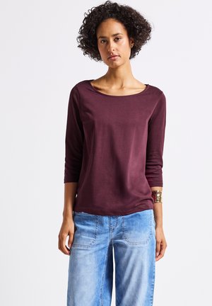 Haut bordeaux à manches longues avec un col bateau, associé à un jean large bleu clair, en tissu texturé et avec des détails de couture subtils.