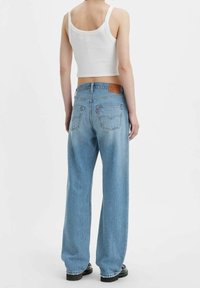 Jeans de mezclilla de corte ancho en azul claro con cintura alta, que cuentan con un parche de cuero en la parte trasera y dos bolsillos traseros. Combinados con una camiseta crop blanca.