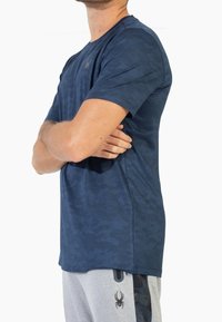 Námořnická modrá sportovní tričko s krátkým rukávem a texturovaným maskáčovým vzorem, s logem na hrudi, vyrobené z lehkého prodyšného materiálu.