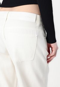 Jeans in denim bianco con taglio dritto, dotati di una tasca sul retro, una patch in pelle bianca con l'etichetta e dettagli di cucitura discreti.