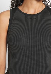 Svart atletisk linne med ribbad textur, ärmlös design och subtil logotyp på övre bröstet. Har kontrasterande tyg vid axlarna.