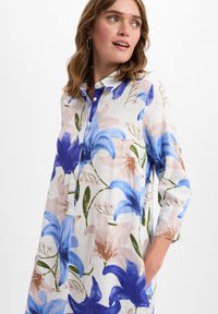 Blumenhemdkleid mit großen blauen und rosa Blumen auf hellem Hintergrund. Entworfen mit einem Knopfleistenkragen und mittel langen Ärmeln.