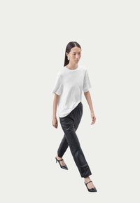 Hvid kortærmet T-shirt i kombination med sorte tapered bukser, der har en glat tekstur og sidelommer, suppleret med sorte hæle.