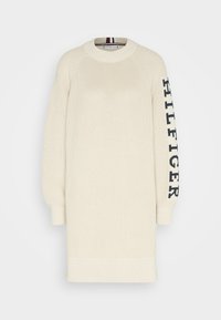 Vestito maglione lavorato a maglia in tonalità bianco sporco, con texture a costine, maniche raglan e un testo logo nero lungo la manica sinistra.