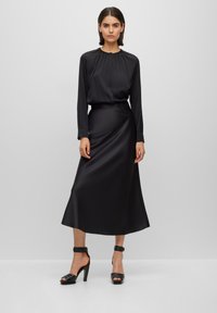 Svart satin långärmad klänning med samlad halsringning och matchande bälte. Öppetåad svart högklackad sandal med ankle straps.