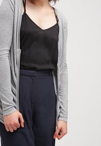 Cardigan gris avec une texture douce, à l'avant ouvert et aux manches longues, superposé sur un débardeur noir. Associe avec un pantalon taille haute bleu marine.