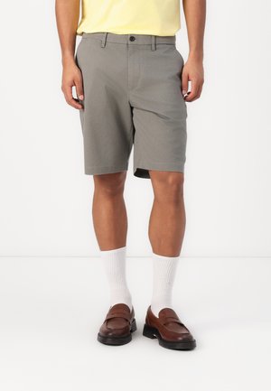 Pantalones cortos grises con diseño de frente plano, cierre de botón y bolsillos laterales. Combinados con calcetines blancos y mocasines marrones. Estilo simple y casual.