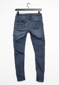 Mörkblå denim skinny jeans hängande, med en slät textur, femficksdesign och diskreta stygnsdetaljer på bakfickorna.