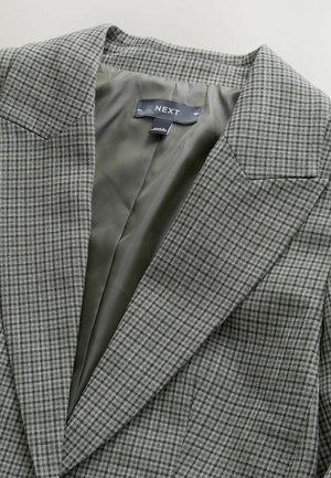 Hall ruuduline bleiser, millel on sile roheline vooder, tähtsa krae ja struktureeritud õlad. Silt kannab nime "NEXT".