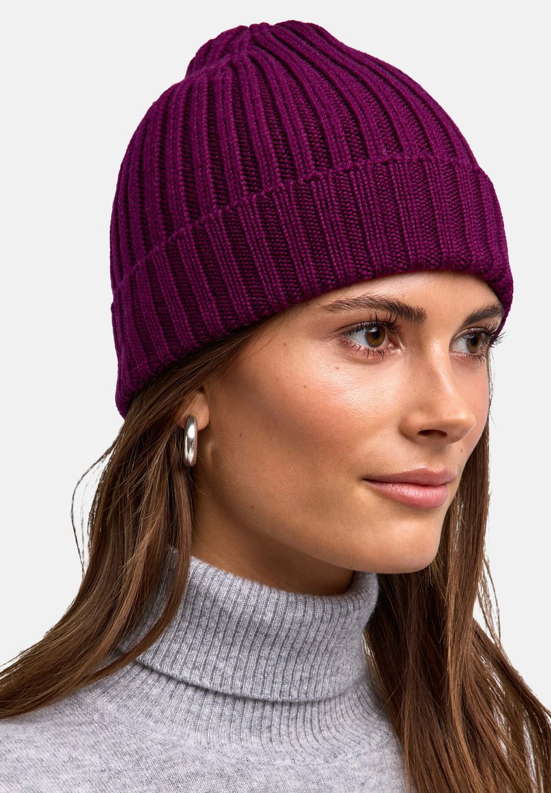 Beanie lavorato a maglia di un profondo viola con una texture a coste verticali. Il design presenta una vestibilità aderente e una parte superiore arrotondata, realizzato in tessuto morbido.