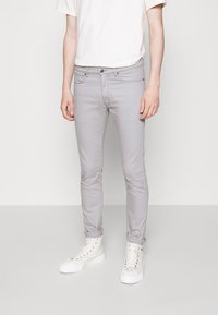 Jeans ajustados de color gris claro, hechos de una mezcla de algodón, con cinco bolsillos y cremallera. Combinados con zapatillas altas blancas.