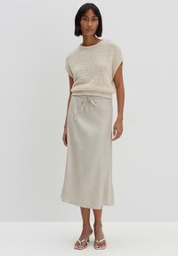 Helles beiges Strickoberteil mit kurzen Ärmeln und Rundhalsausschnitt, kombiniert mit einem bodenlangen Leinenrock mit Kordelzugbund. Silberne Sandalen.