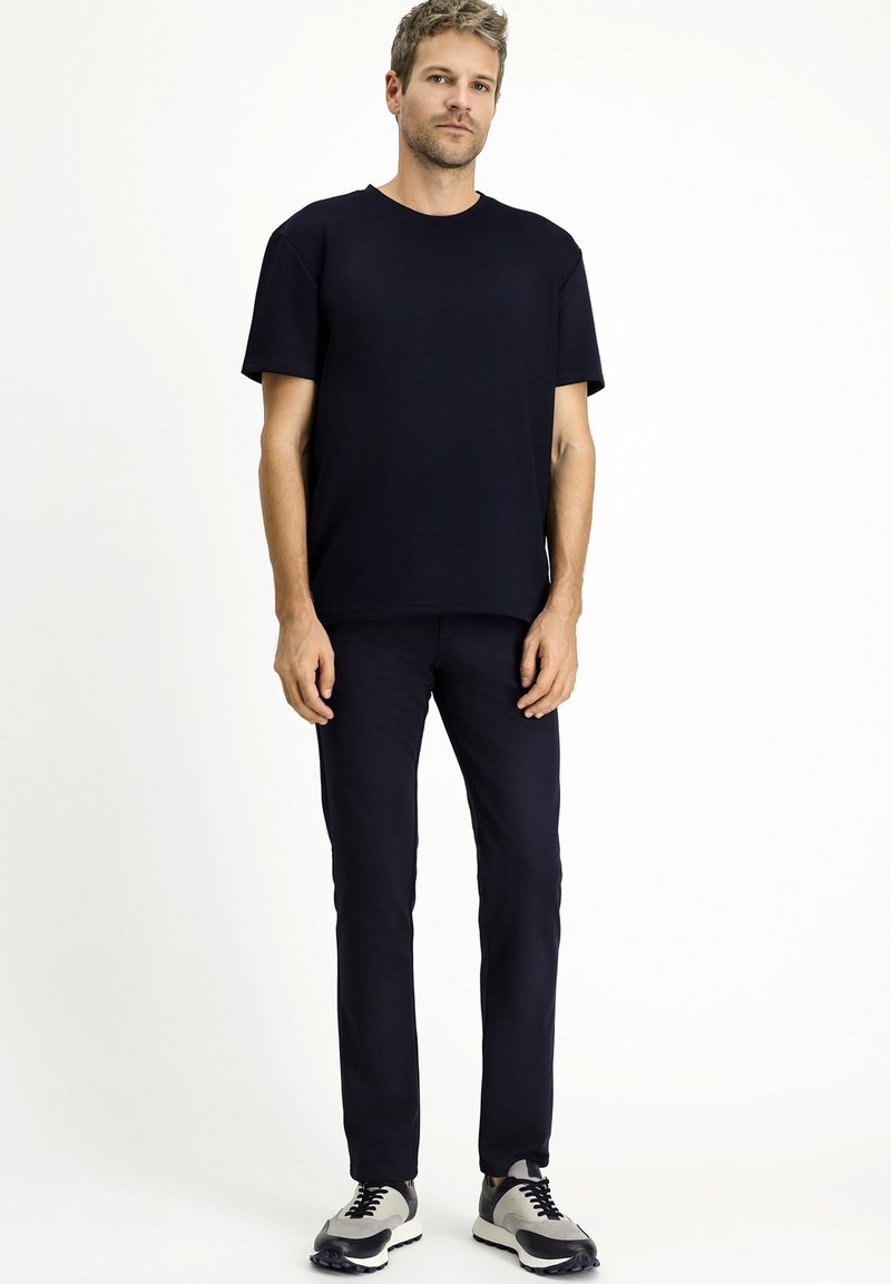 Camiseta de manga corta azul marino combinada con pantalones azul marino y zapatillas grises. El conjunto tiene un diseño simple y estilizado, con una textura suave.