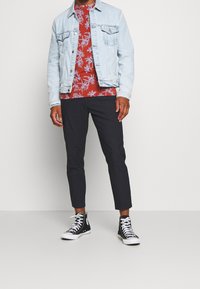 Light blue denim jacket, red floral shirt, black tapered pants, and black high-top sneakers. Features include two chest pockets and white laces.