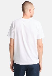 Camiseta blanca de algodón con mangas cortas, cuello redondo y espalda lisa. Textura suave, corte estándar y sin patrones ni gráficos visibles.