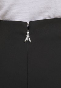 Falda negra ajustada con cierre de cremallera plateado en la parte posterior, que presenta un tirador de cremallera decorativo que recuerda a hojas estilizadas.