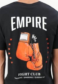 Sort t-shirt med grafisk tryk af orange boksehandsker, "EMPIRE" og teksten "FIGHT CLUB TRAINING / SPARRING / QUEENS NY" i hvid. Røde stjerner på siderne.