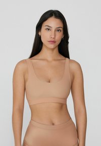 Hladká nude sportovní podprsenka s kulatým výstřihem a širokými ramínky. Měkký, elastický materiál s širokým pásem na spodní části pro podporu.