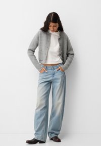 Light gray knitted cardigan with buttons, worn over a white shirt. Paired with loose light blue jeans and dark footwear.
