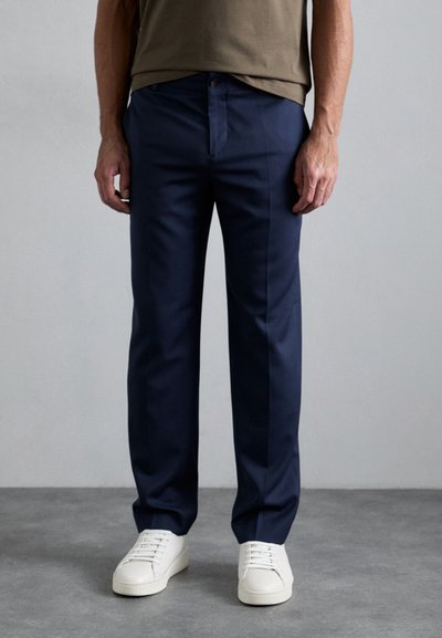Pantaloni blu navy con vestibilità dritta, dotati di tasche frontali e chiusura con bottone, abbinati a sneakers bianche basse.