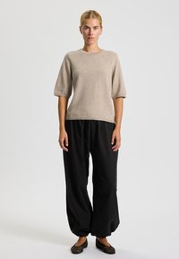 Maglione beige a maglia con maniche corte abbinato a pantaloni neri larghi. I pantaloni hanno un elastico in vita e polsini arricciati alla caviglia.