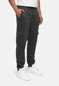 Dark gray joggers made of soft fabric, featuring side pockets and a drawstring waistband, paired with white athletic shoes.