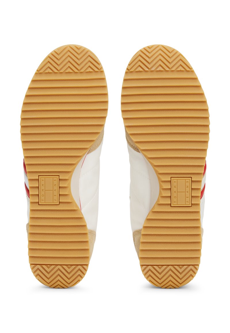 Suelas de zapatillas deportivas blancas con una parte inferior de goma texturizada, que presenta patrones de espiga y un logotipo de la marca. Acabadas en gamuza beige.