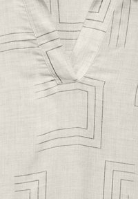 Tissu en lin de couleur claire avec un col en V et des motifs géométriques discrets en gris. Texture douce avec un léger éclat.