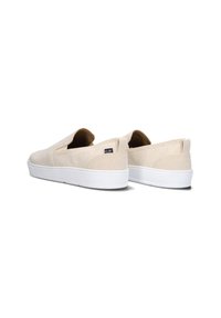 Beige canvas instappers met een witte rubberen zool, met een lage profiel, subtiele stiksels en een klein merkembleem op de zijkant.
